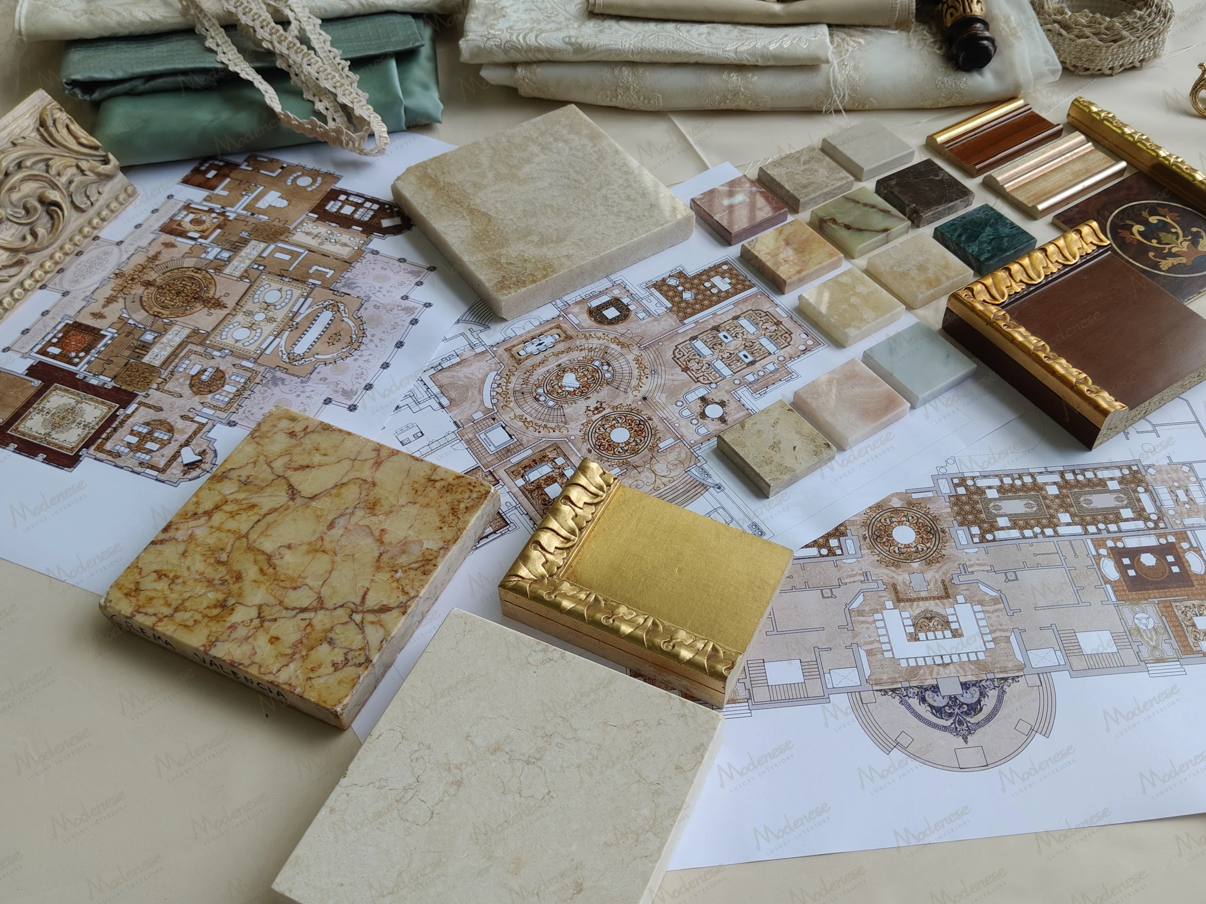 Milan design studio presentation of marble and wood samples overlaid on detailed interior floor plans and ornamental drafts