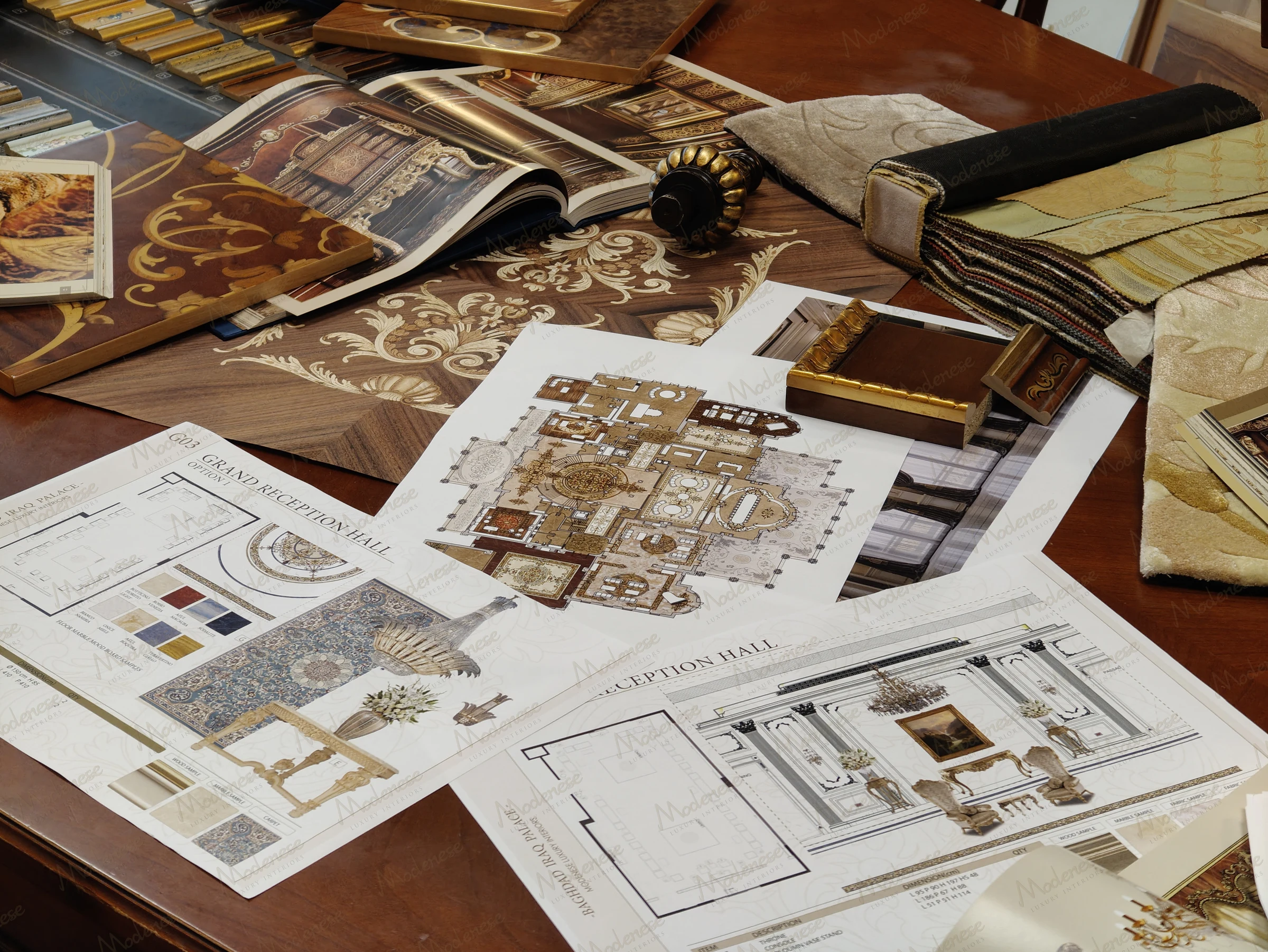 Close-up of Modenese  design studio table filled with grand reception hall blueprints, wood inlay samples, fabric swatches, and gold hardware