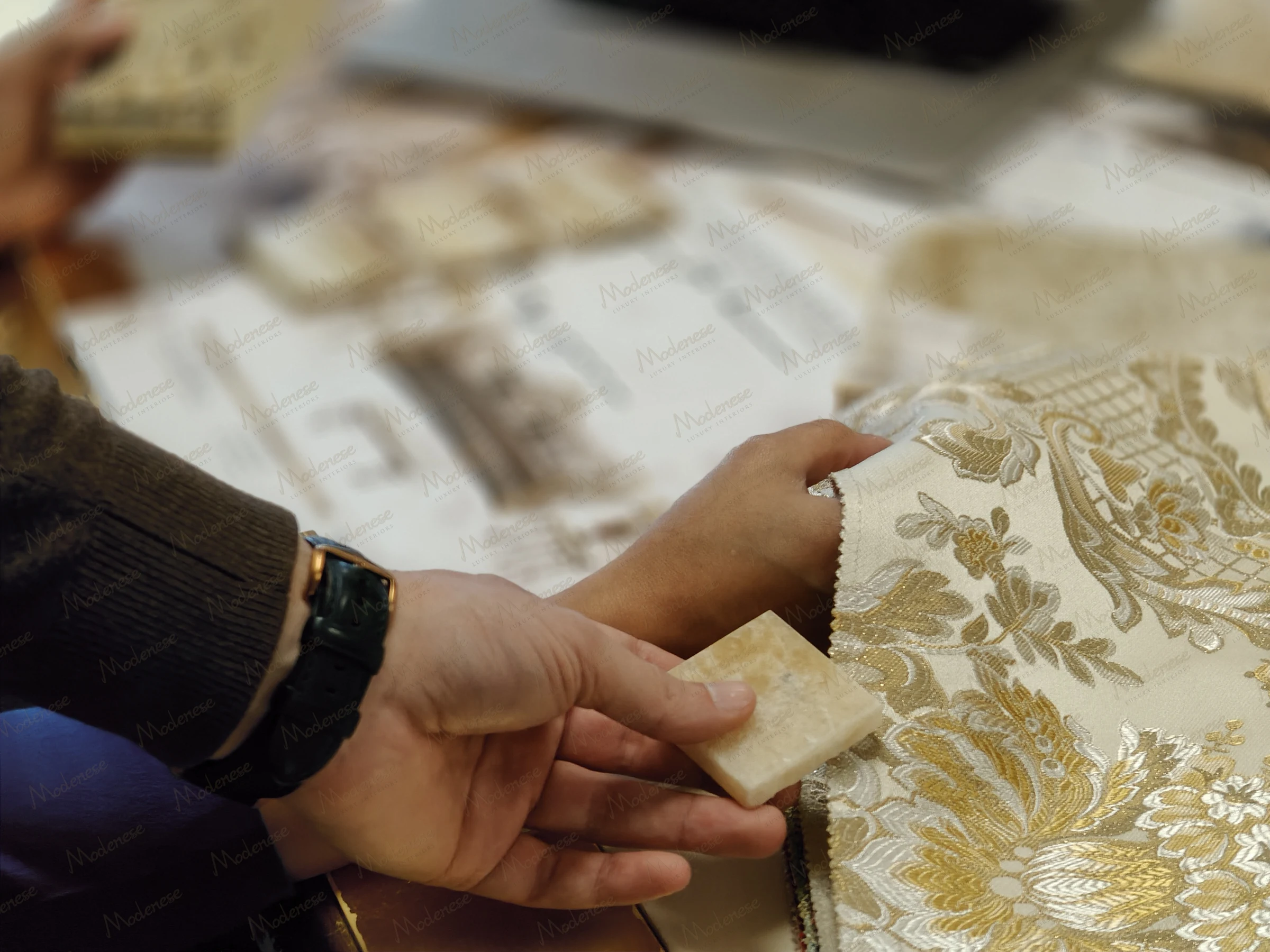 Hands comparing a marble tile with luxurious gold and cream damask fabric in a Virginia interior design consultation session