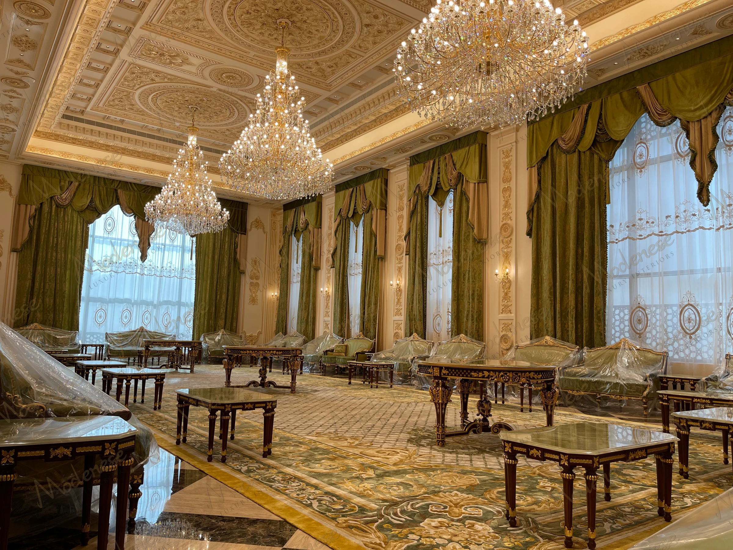 Lavish reception room in Saudi Arabia King's Palace featuring crystal chandeliers, green and gold draped curtains, and classic wooden tables with plastic-covered seating
