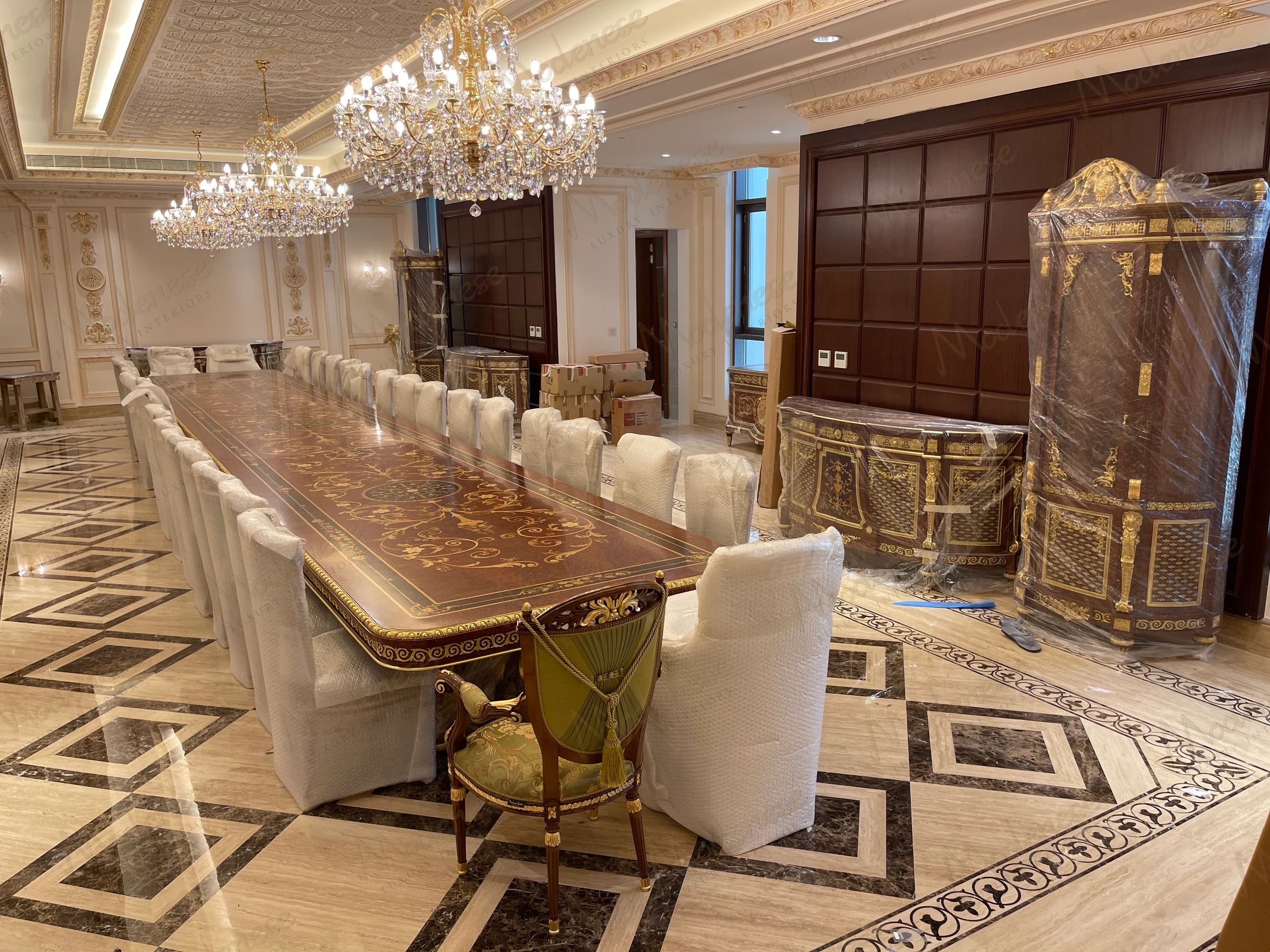Formal dining room in Saudi Arabia King's Palace with a long inlaid wooden table, upholstered chairs wrapped for delivery, and opulent gold-trimmed cabinetry