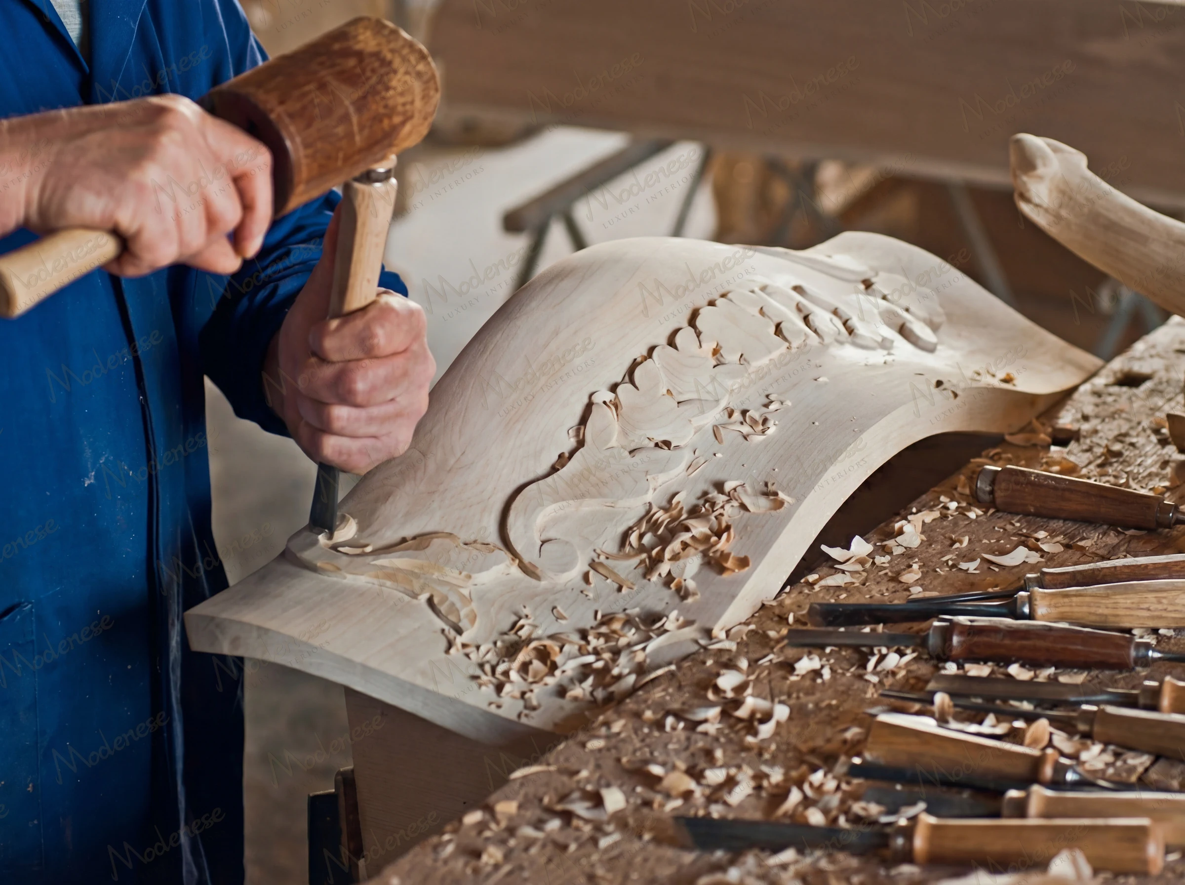 Artisan hand-carving intricate floral details into a curved wooden furniture panel at Modenese Interiors