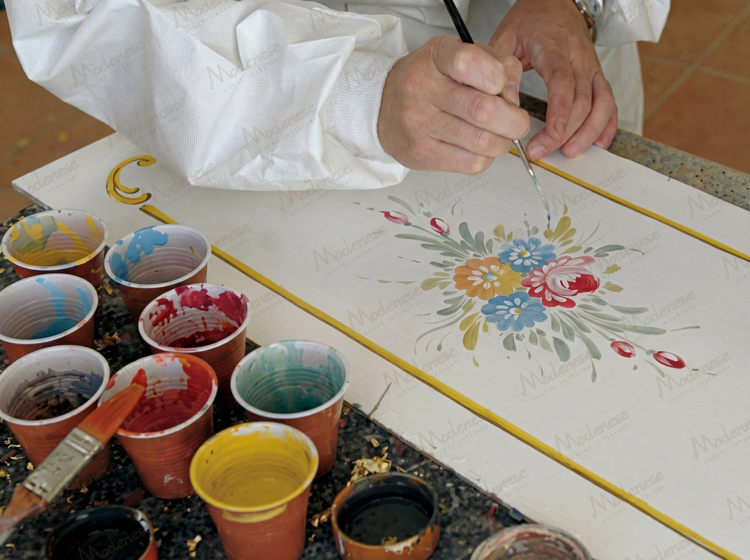 Hand-painting a floral design on a furniture panel with vivid pigments at Modenese Interiors manufactory
